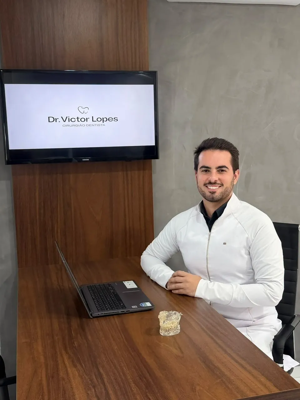 Dr. Victor Lopes em sua sala de consulta, com a marca do consultório ao fundo